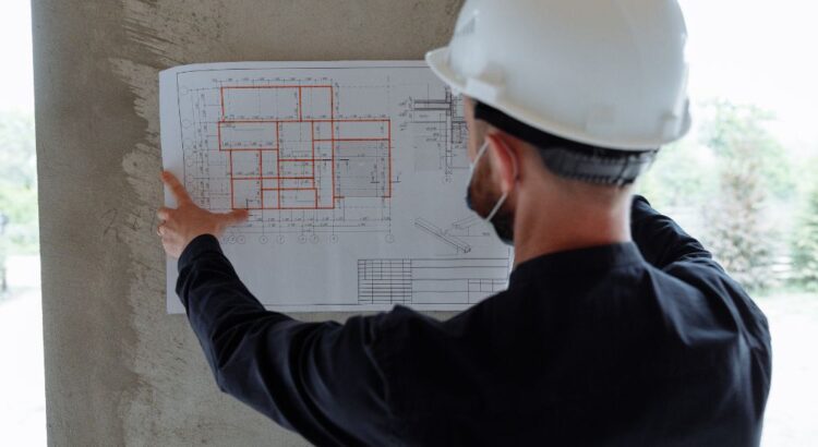 Arquiteto analisando planta técnica em obra, ilustrando quanto um arquiteto ganha por projeto, com foco em planejamento, execução e valorização do trabalho profissional.